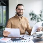 persona-revisando-documentos-y-computadora-abierta